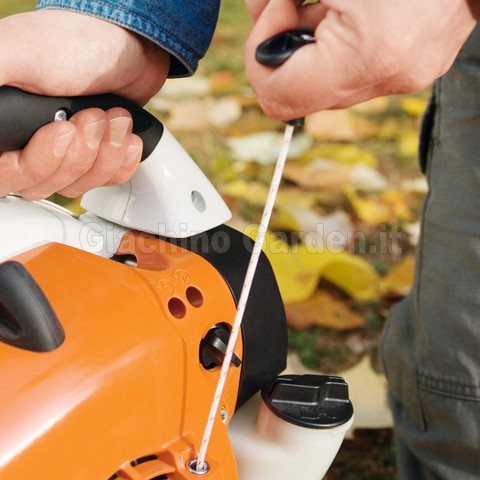 Persona che avvia un soffiatore Stihl tirando la fune di avviamento con impugnatura ElastoStart, tenendo salda la maniglia superiore del macchinario arancione.