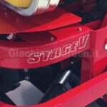 Dettaglio della carrozzeria rossa di un trattorino Gianni Ferrari Turbo 1-2 con la scritta adesiva 'STAGE V' in evidenza. L'etichetta certifica la conformità del motore alle più recenti e restrittive normative europee sulle emissioni inquinanti. Si notano i componenti meccanici neri del telaio e la finitura lucida della scocca professionale.