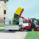 Trattorino rasaerba professionale Gianni Ferrari Turbo 1 in funzione: il braccio idraulico solleva il capiente cesto di raccolta giallo per scaricare l'erba tagliata direttamente nel cassone di un autocarro