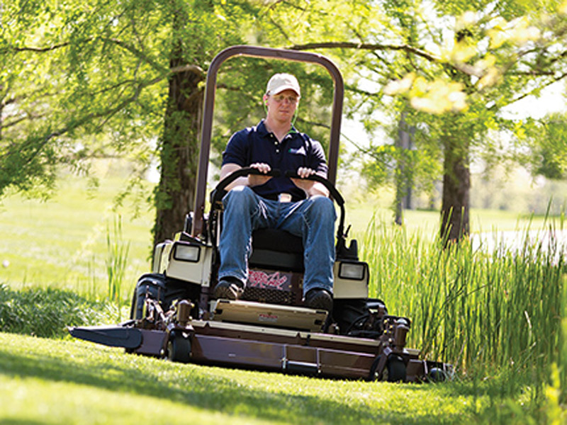 Operatore alla guida di un trattorino Grasshopper mentre taglia l’erba in un’area verde con vegetazione alta