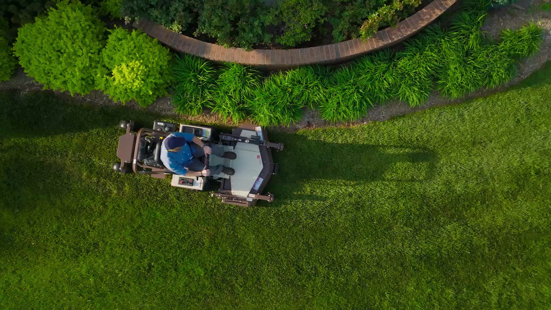 Vista dall'alto di un trattorino rasaerba professionale a raggio zero guidato da un operatore mentre taglia l'erba di un prato curato