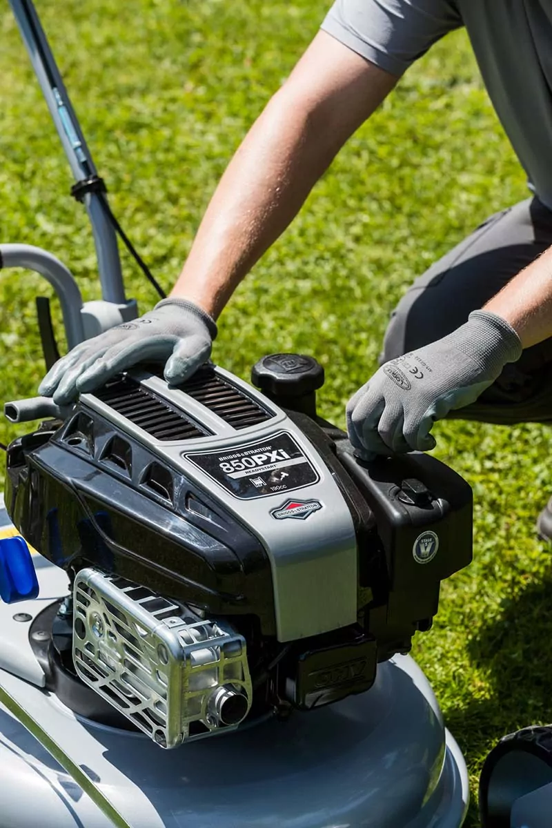 Dettaglio del potente motore Briggs & Stratton 850PXi montato su un tagliaerba Grin, con un operatore che ne verifica i componenti in un prato.