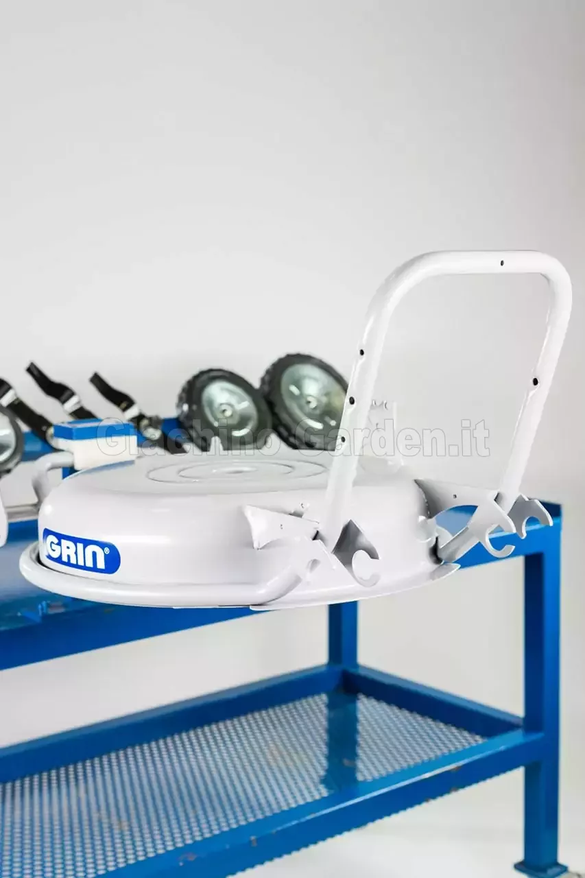 Dettaglio del piatto di taglio Grin con logo in evidenza e stegola di guida, poggiato su un banco da officina professionale blu.