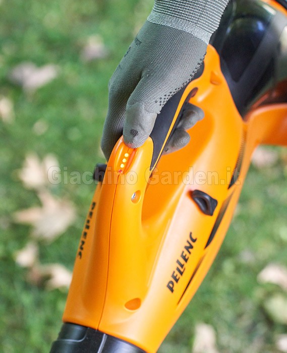 Primo piano dell’impugnatura del soffiatore professionale Pellenc Airion 3, azionato da un operatore con guanti da lavoro su prato con foglie, evidenziando ergonomia e controllo durante la manutenzione del verde.