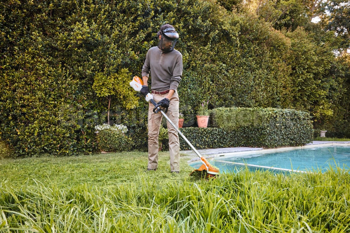 Giardiniere utilizza il decespugliatore a batteria Stihl FSA 110 R per tagliare l'erba alta a bordo piscina in giardino.